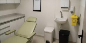 PGRSS na clínica: sala de procedimentos com coletor de perfurocortante fixado no suporte de parede, lixeiras com tampa e pedal e pia para higienização das mãos